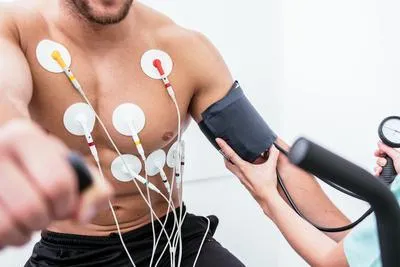 Man on a stationary bike with EKG electrodes and a blood pressure cuff.