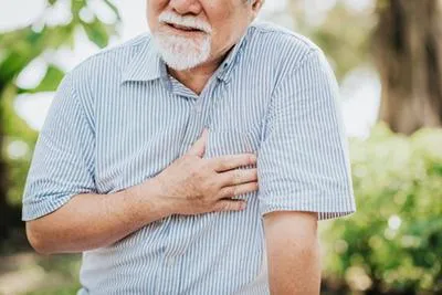 An elderly man clutching his chest in pain while standing outdoors.