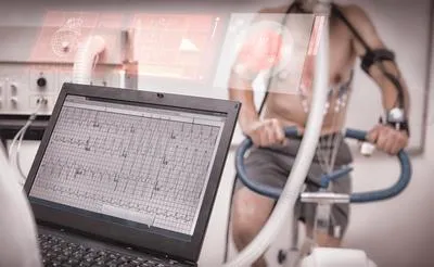A person undergoing a cardiac stress test on a stationary bike while a laptop displays their EKG readings.