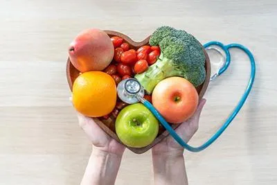 Hands holding a heart-shaped bowl of produce with a stethoscope.