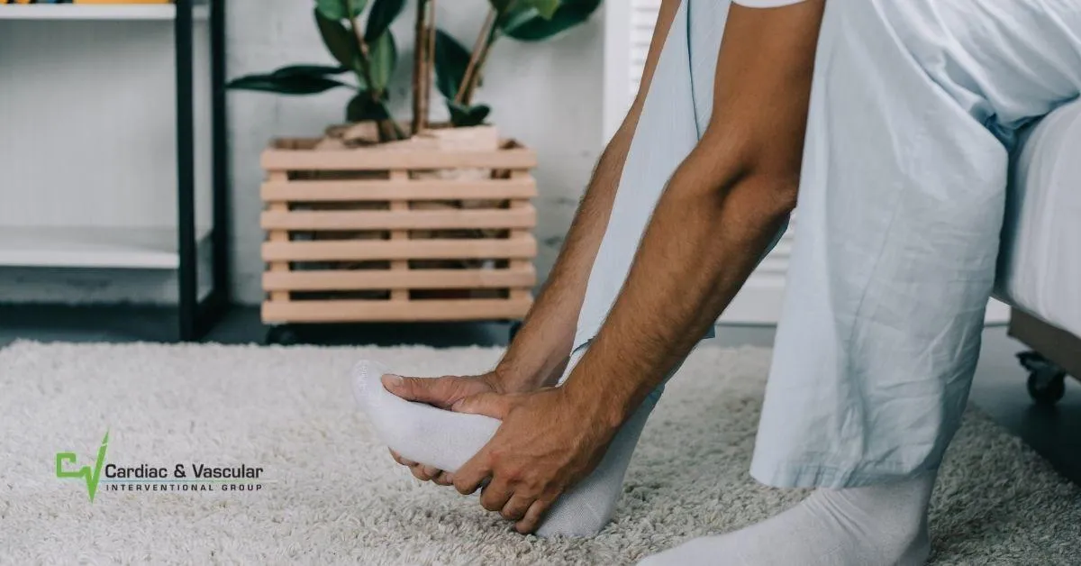 A person in medical scrubs sitting on the edge of a bed and holding their foot in pain.