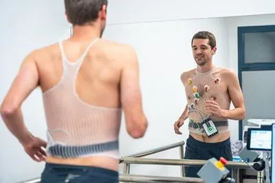 A man wearing a cardiac monitor vest while running on a treadmill during a medical stress test.