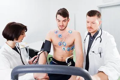 Man undergoing a cardiac stress test while monitored by two medical professionals.