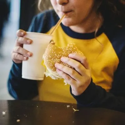 A person wearing a yellow and navy blue long-sleeve shirt holding a sesame seed burger with a bite taken out of it.