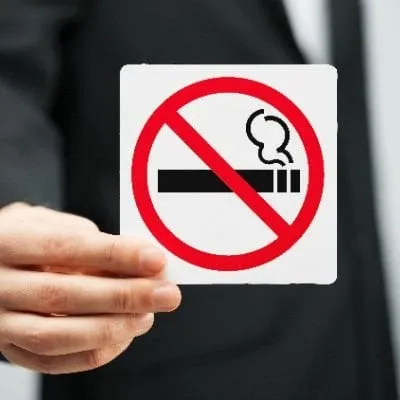 A person's hand holding a small white square card with a red "no smoking" symbol.