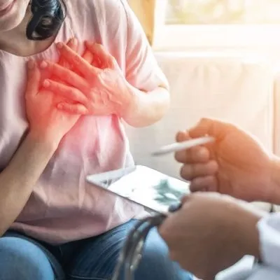A woman clutching her chest with a red glow indicating pain while a doctor holds a tablet and pen.