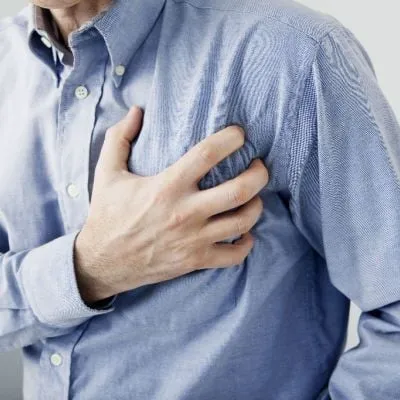 A man in a blue button-down shirt clutching his chest in pain.