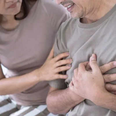 A man clutching his chest in pain while a woman places a supportive hand on his arm.