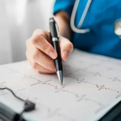 A healthcare professional in blue scrubs holding a black pen over a clipboard.