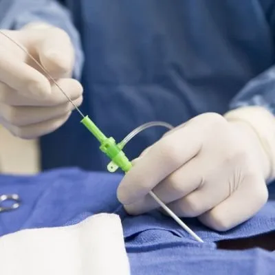 A surgeon's gloved hands performing a catheterization procedure.
