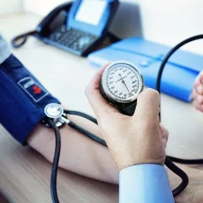 A healthcare professional's hand holding a manual sphygmomanometer gauge while checking a patient's blood pressure.